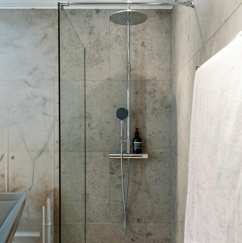 Large rain shower head with wand sprayer in marbled shower.